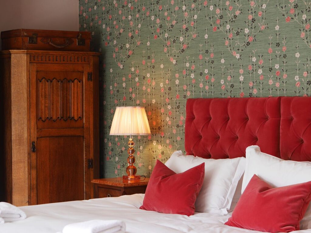 A cozy room in an English country pub with a gorgeous red headboard and floral wallpaper