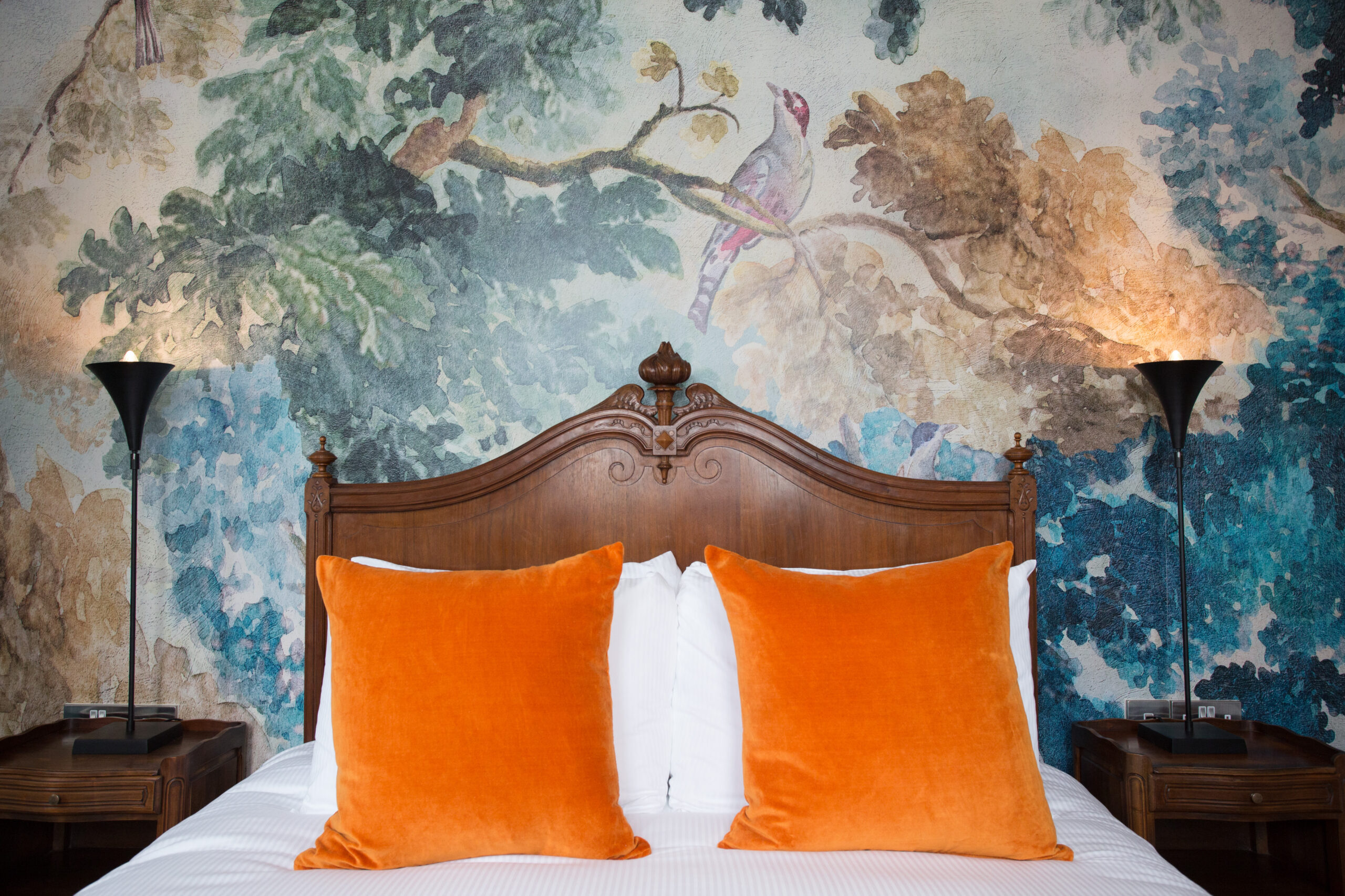 A king size bed with a old wooden headboard and orange velvet pictures. 
